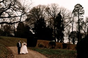 A couple walking hand in hand on an autumn path surrounded by tall trees and hedges at dusk.
