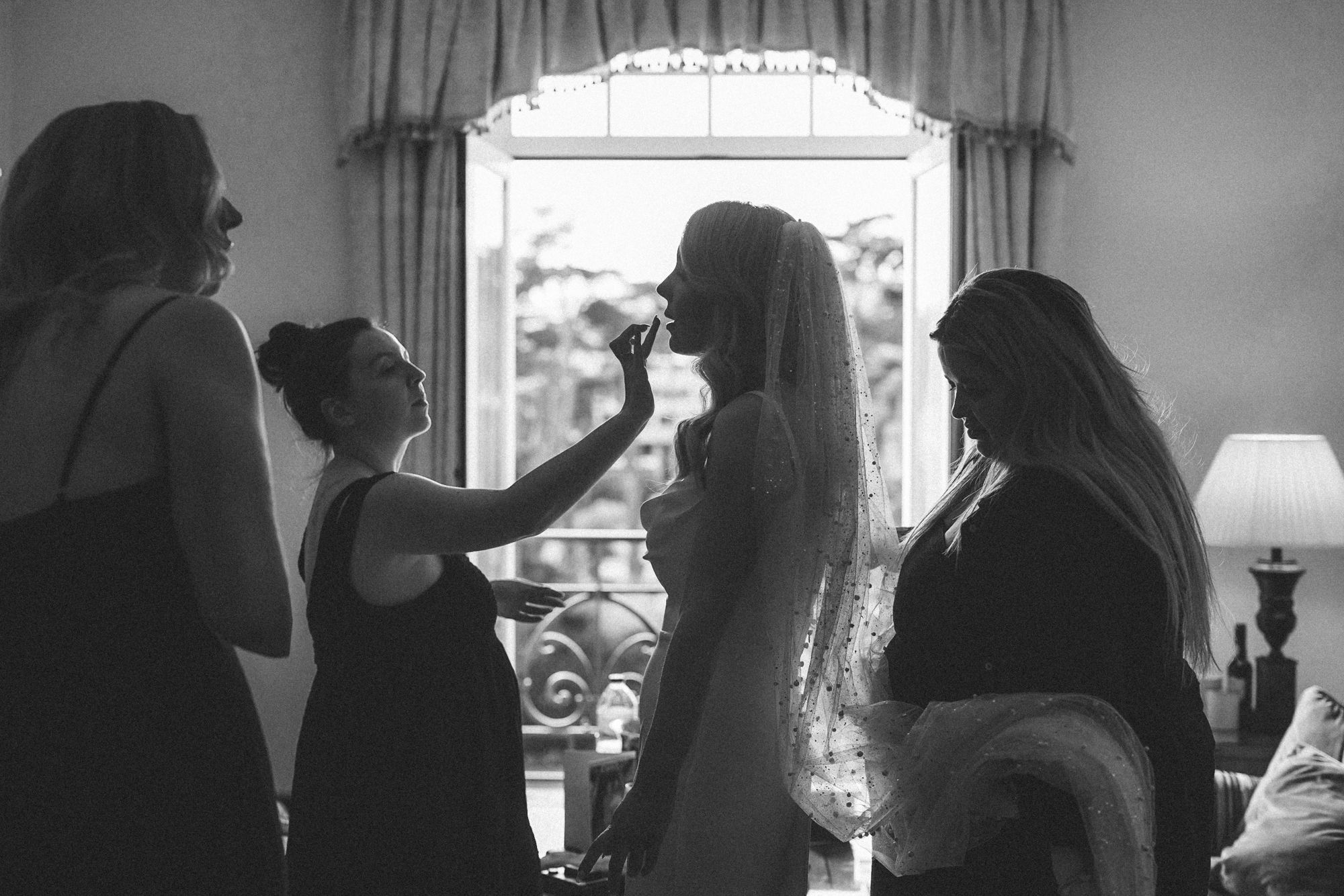 Black and white image of wedding preparation scene near window at hotel palacio. captured by a destination wedding photographer in portugal