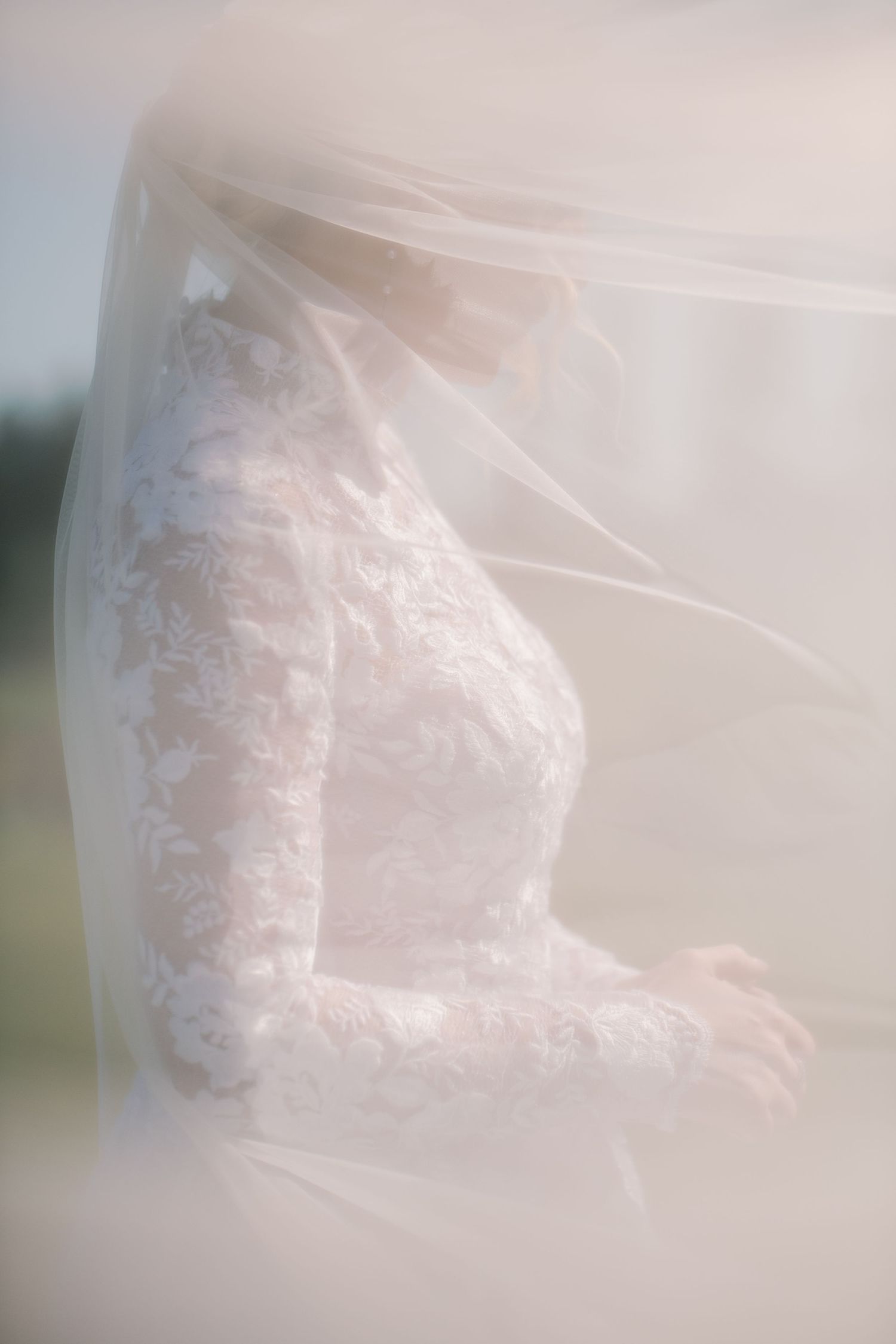 A soft, ethereal close-up of delicate white lace details on a wedding dress through sheer veil material.