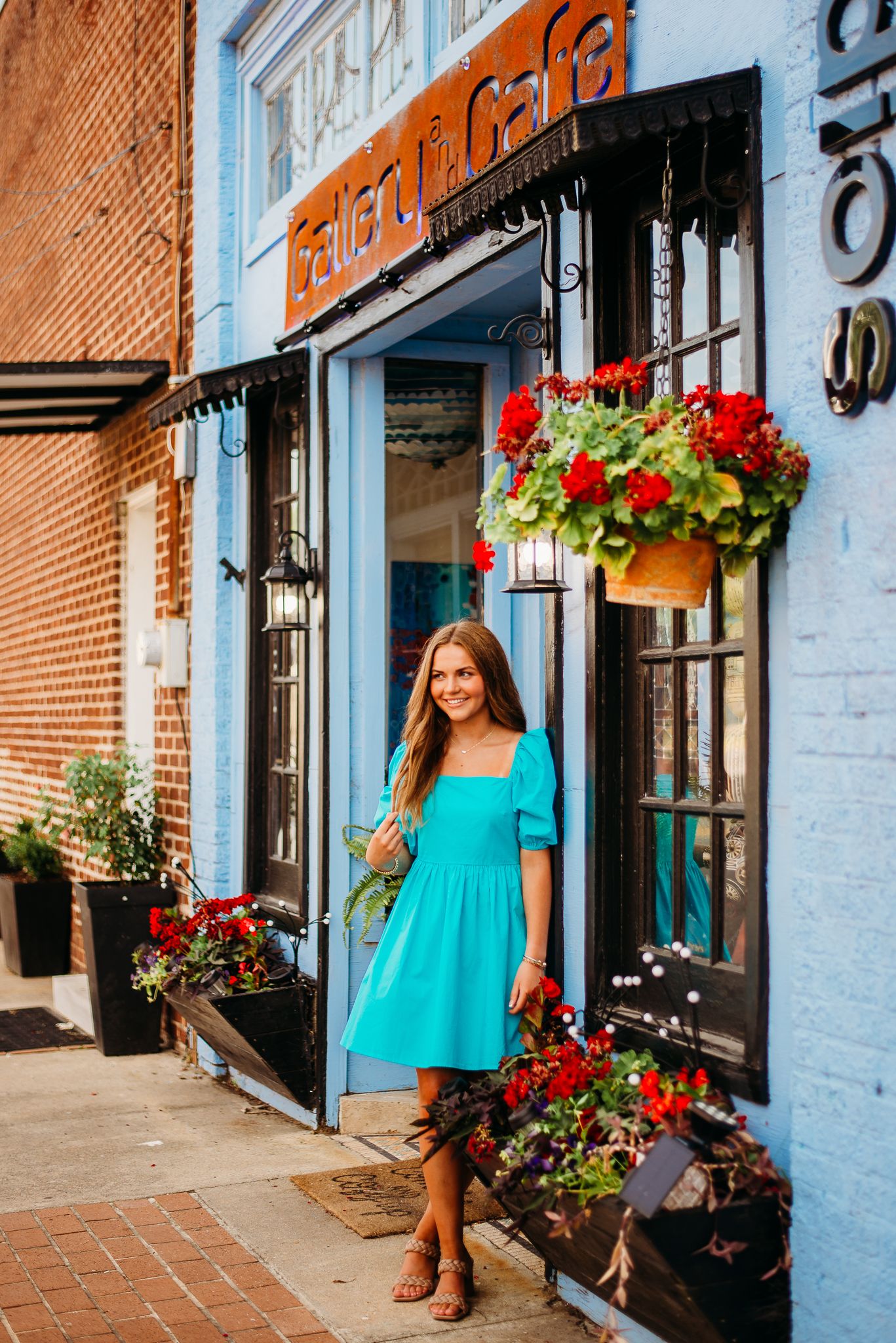 A summery turquoise dress outfit photographed in front of a charming storefront with red flowers.