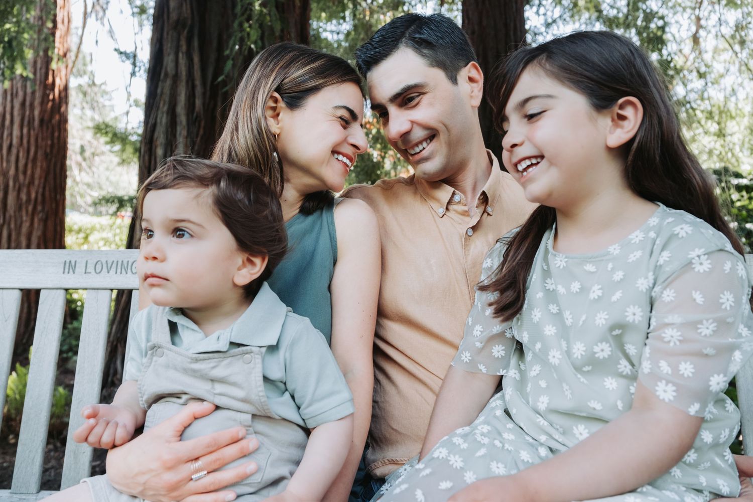 A close-knit family group smiles together outdoors on a sunny day.