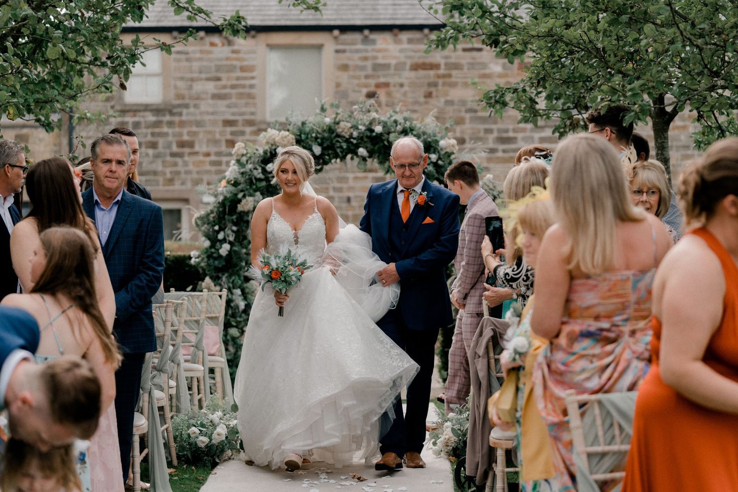Wedding ceremony processional with floral decorations and outdoor garden setting.