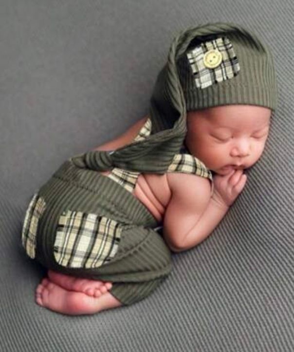 Sleeping newborn wearing olive green knit cap and wrap against gray backdrop.