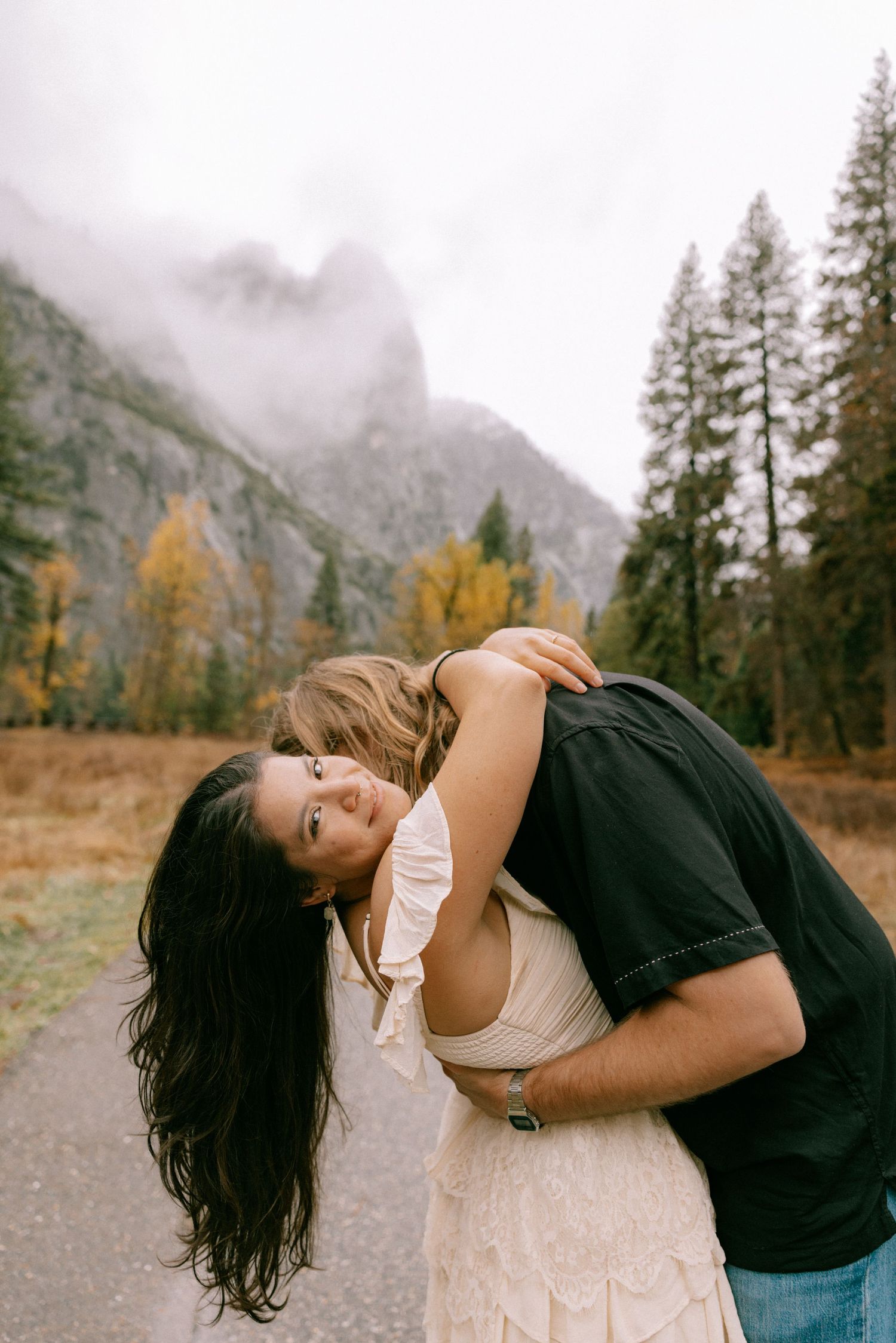 A romantic couple embraces against a misty mountain backdrop with autumn trees in Yosemite Valley.