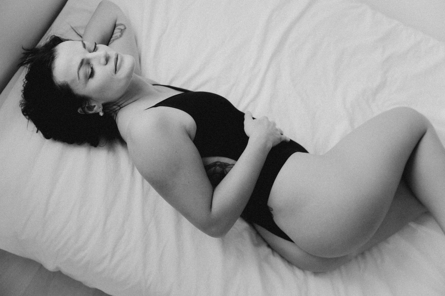 Boudoirkuva nainen makaa valkoisissa lakanoissa