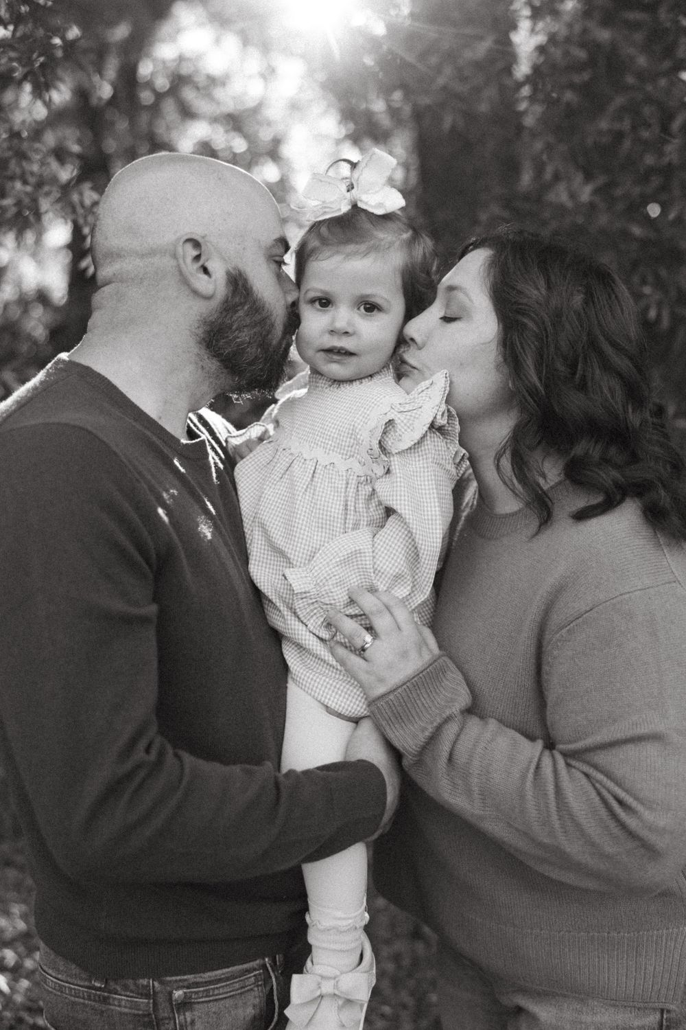 Four sequential black and white photos show tender family moments with a small child in a white dress.