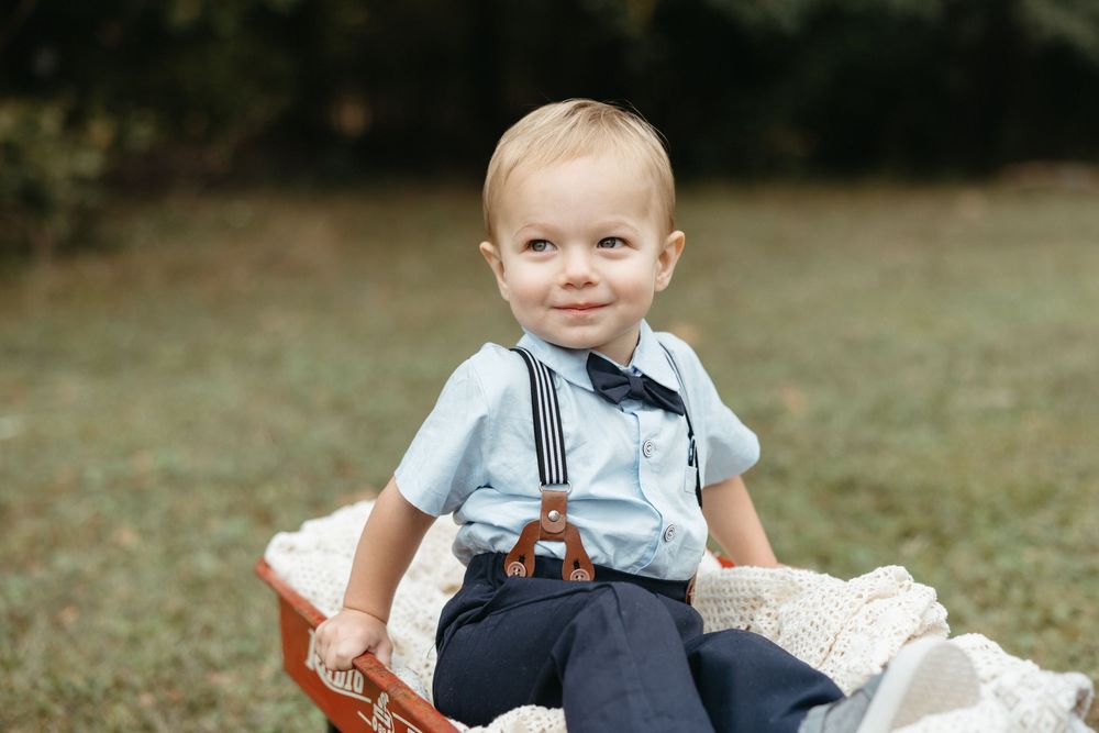 A child in overalls sits on a blanket outdoors while playing with a toy on a sunny autumn day.