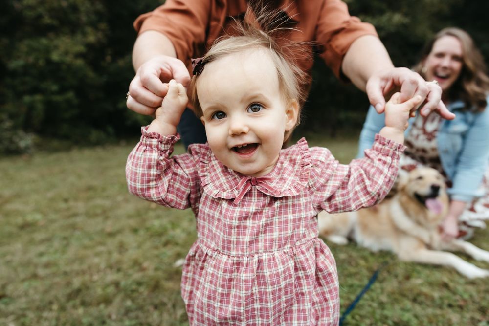 A toddler in a red plaid shirt laughs and plays outdoors on a sunny day.