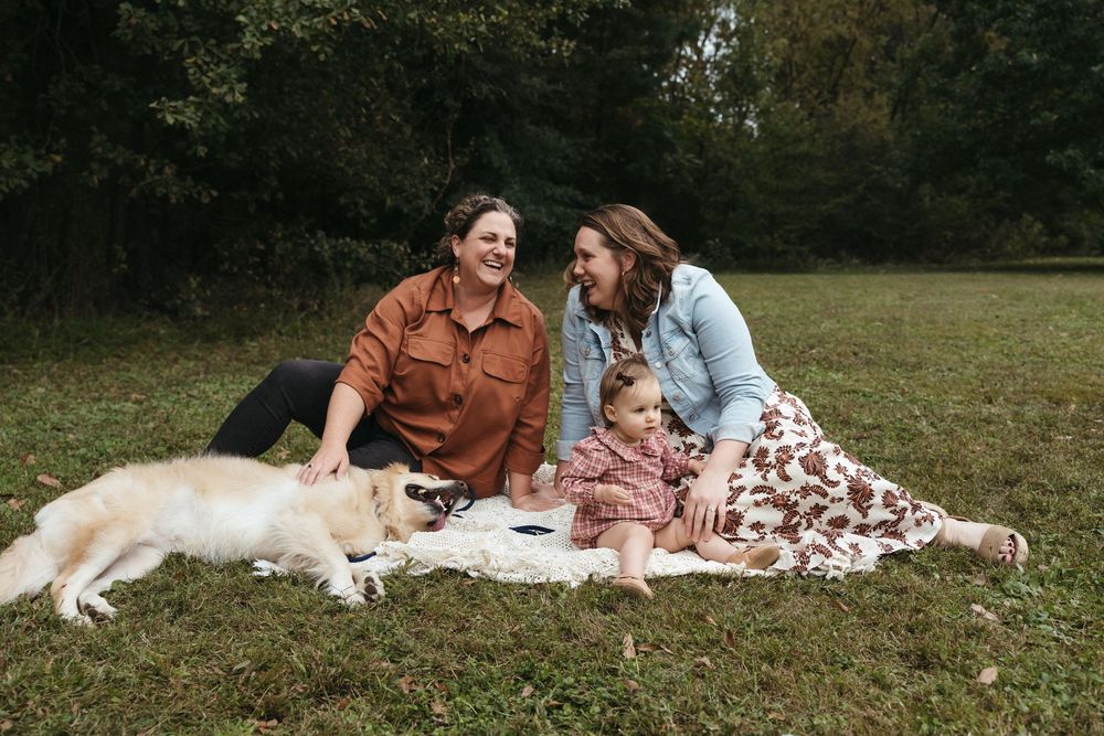 A couple enjoys a romantic picnic on a blanket in a grassy field on a sunny autumn day.