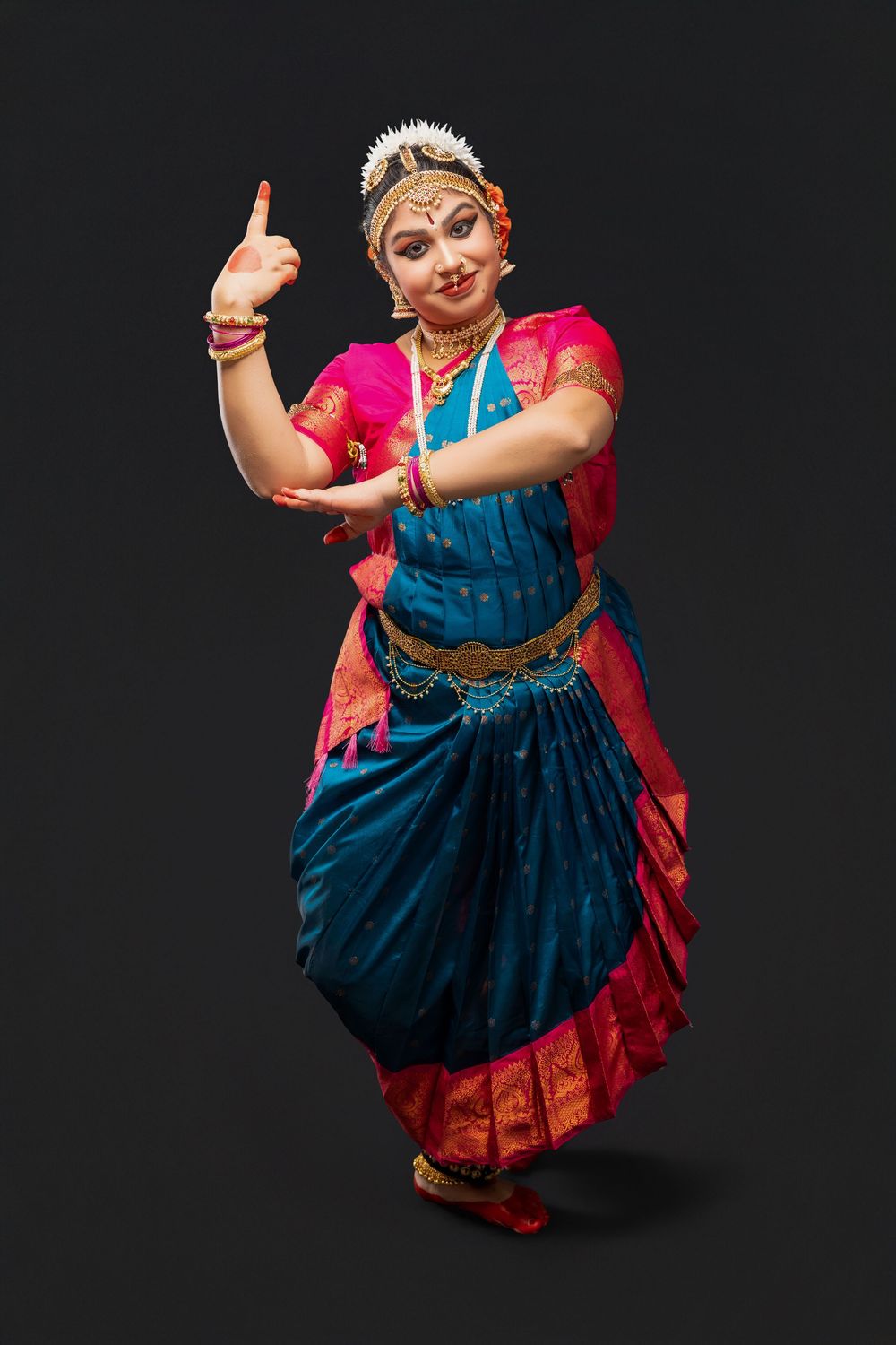 Bharatanatyam dancer strikes graceful pose wearing traditional blue and red costume with jewelry.