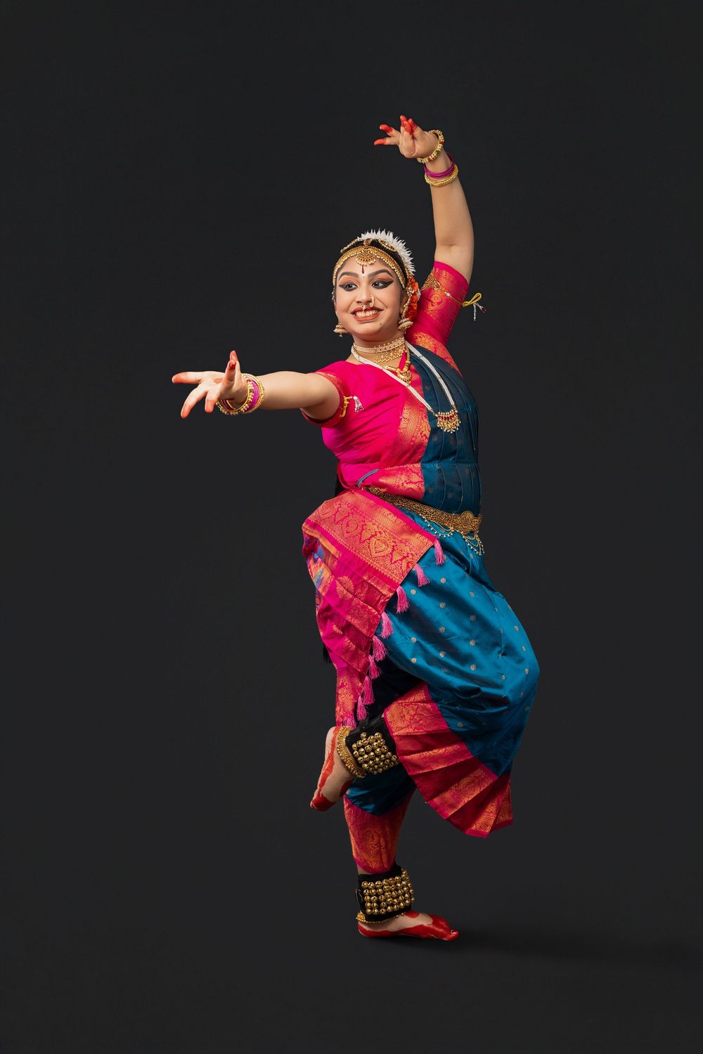 Classical Indian dancer performs in vibrant pink and blue traditional costume against black background.