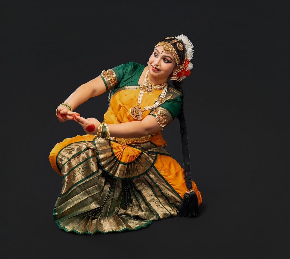 Classical Indian dancer in yellow and gold costume performs expressive hand gestures against dark background.