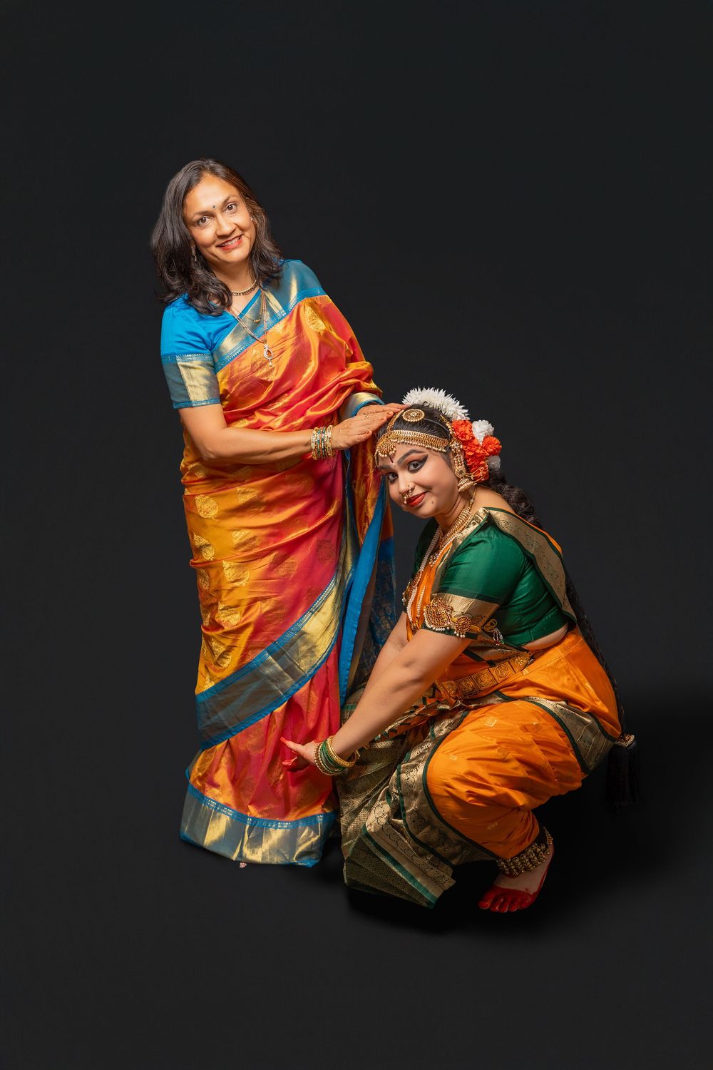 Two people in colorful traditional Indian attire embrace and laugh against a dark background.