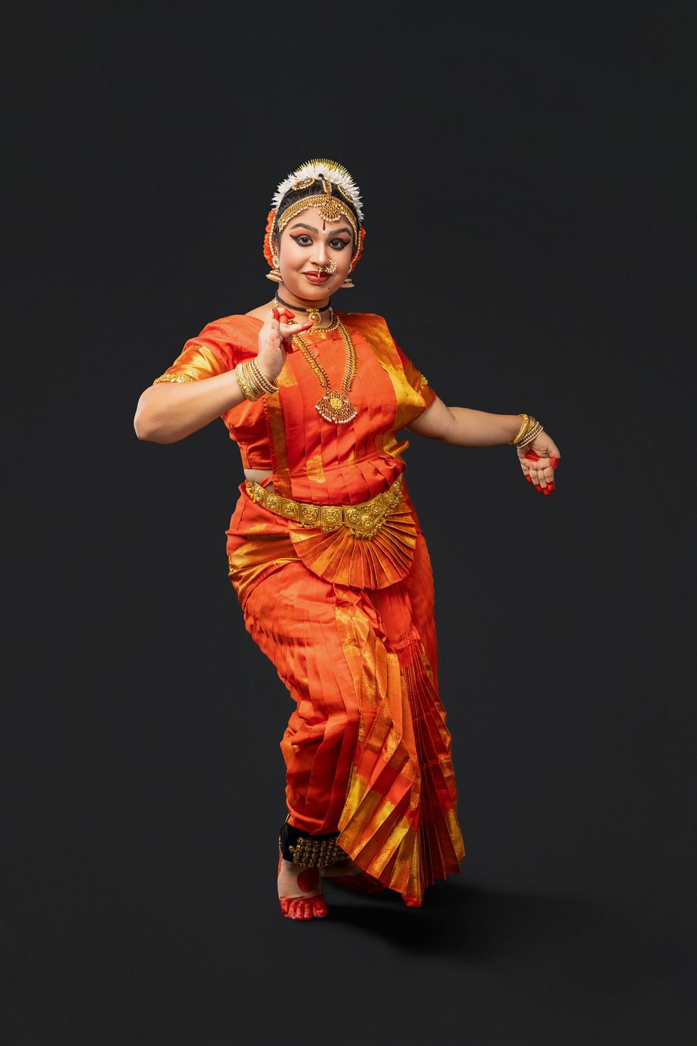 Traditional dancer performs expressive movements in bright orange and gold classical Indian attire.