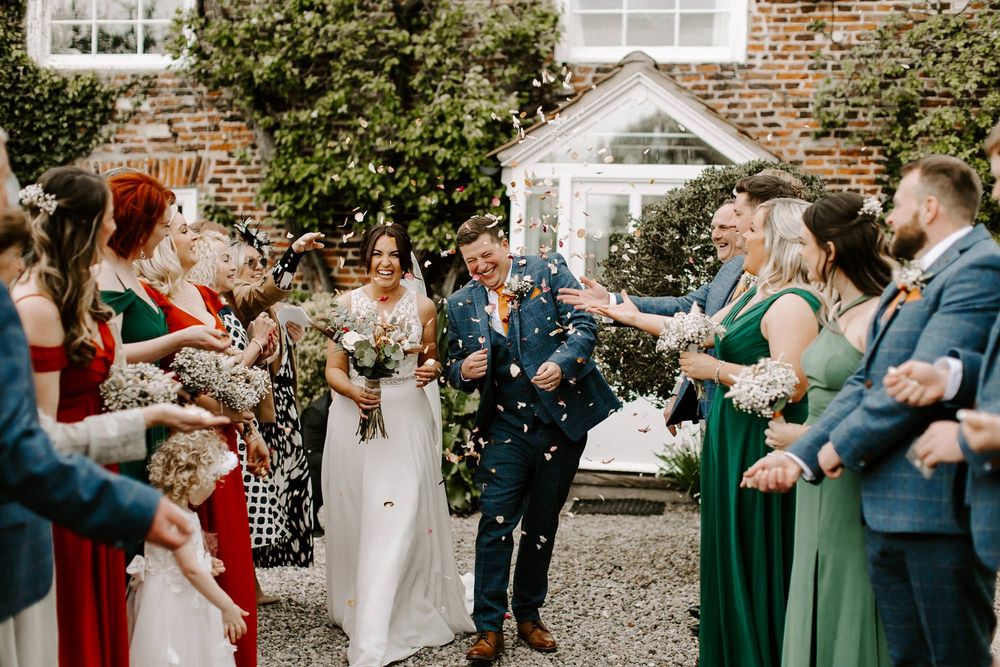 Wedding guests throw confetti over newlyweds outside a brick building during a joyful celebration.