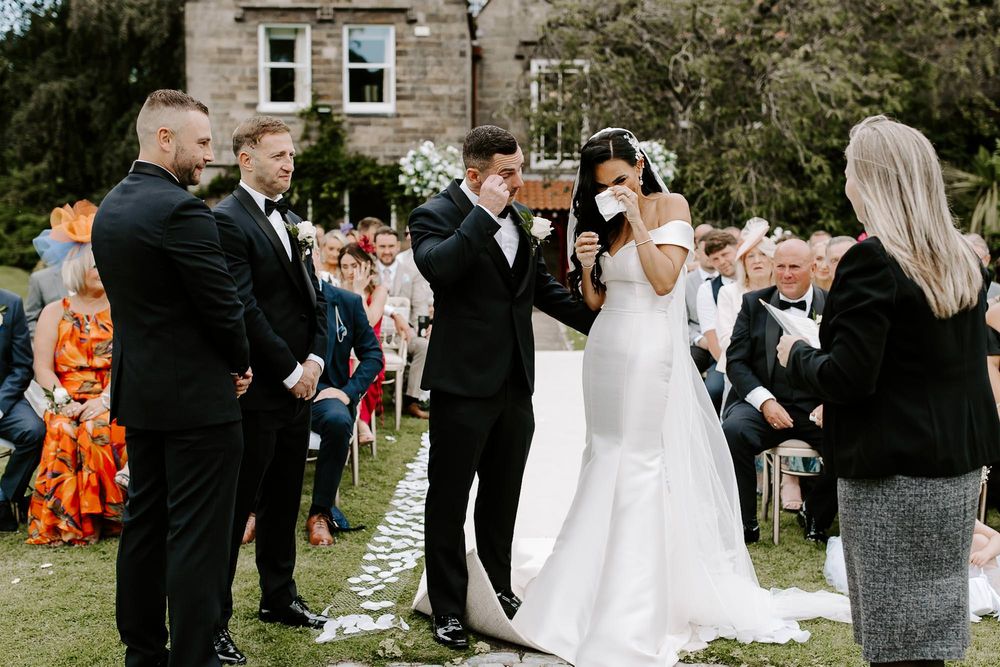 Wedding guests line up outdoors to congratulate the newlyweds during a receiving line at a garden ceremony.