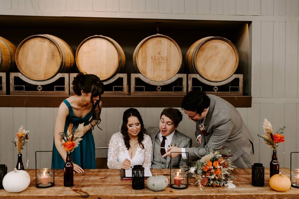 People enjoying drinks and conversation at a rustic winery tasting room with wooden barrels in the background.