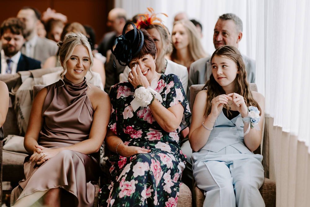 Wedding guests showing emotional reactions during ceremony while sitting in rows of white chairs.