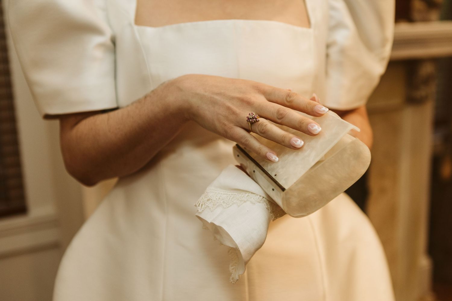 A person in a white dress holds a glass of champagne while standing in an elegant indoor setting.