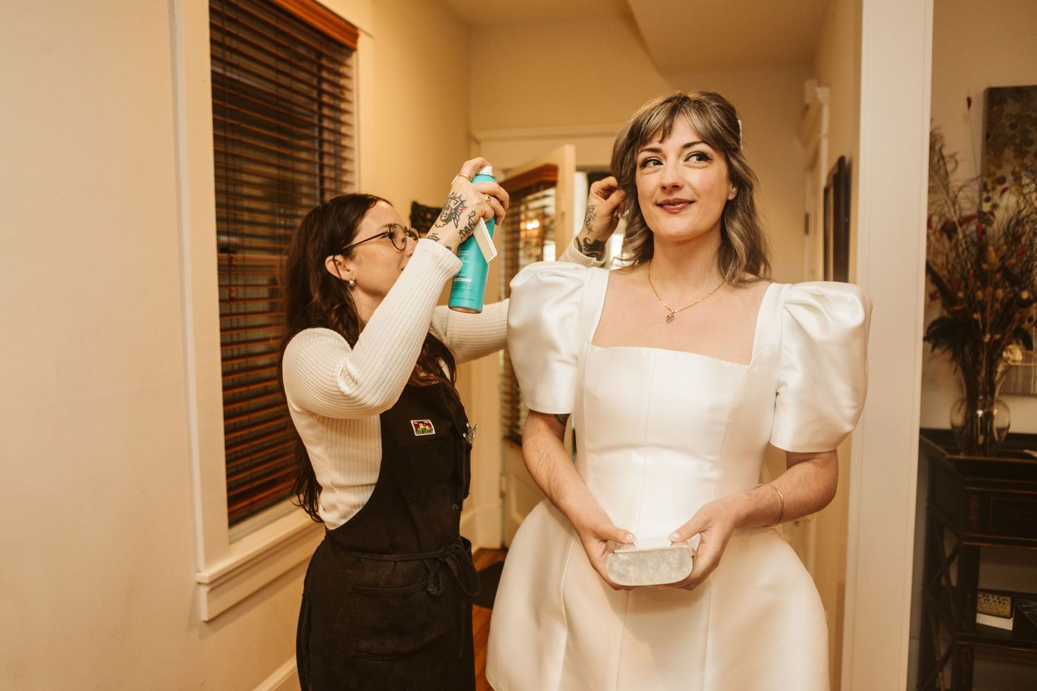 Wedding party members in white dresses share celebratory drinks and laughter during a reception.