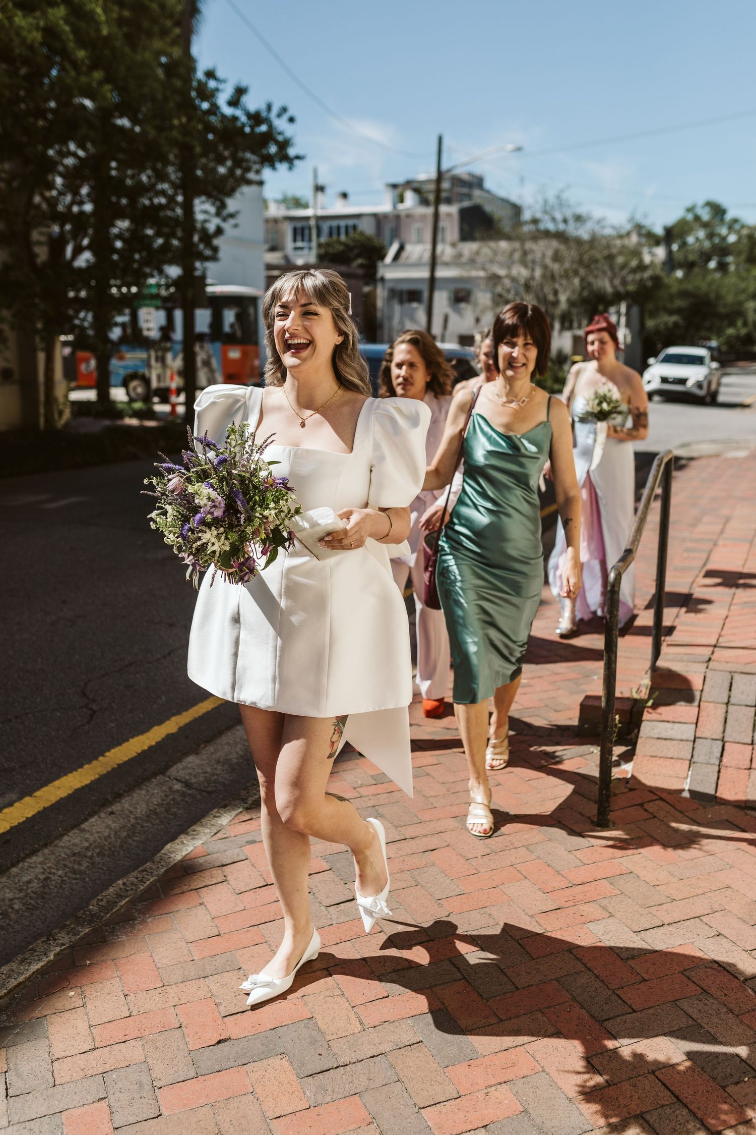 Wedding party walking and laughing together on brick sidewalk in casual summer attire.