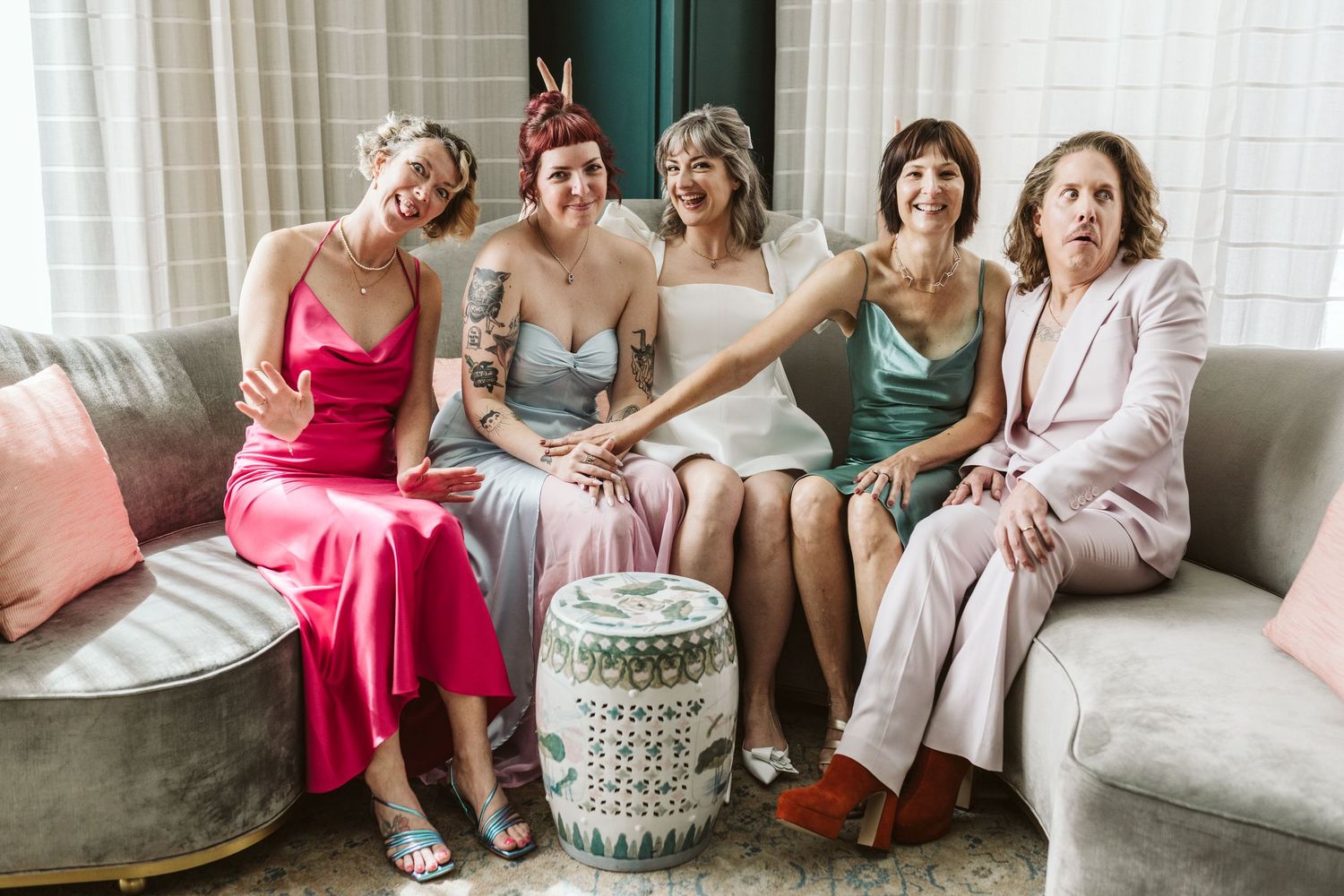 A group of people sitting and laughing together on a gray couch during a casual indoor gathering.