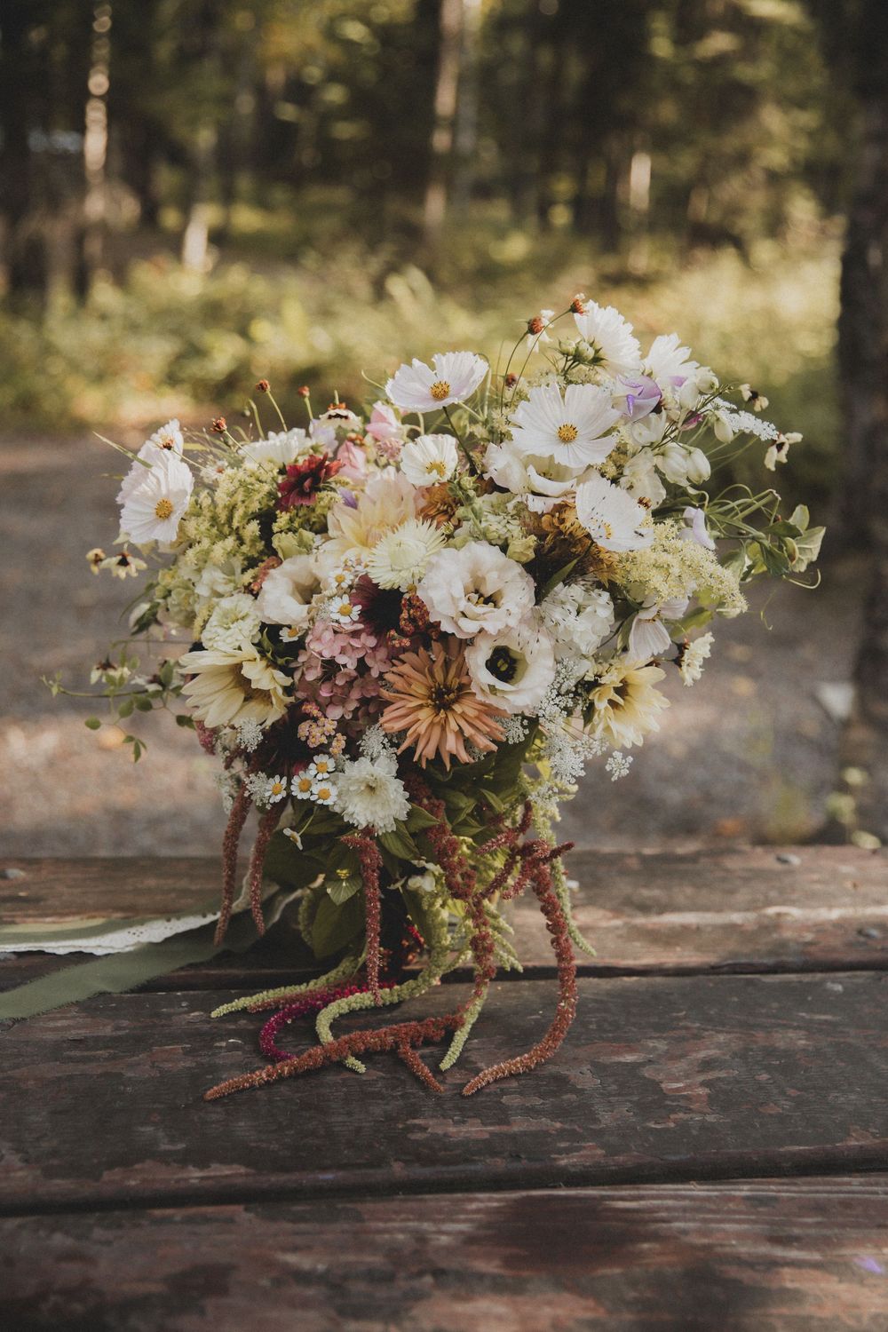 Rustic floral arrangement with white daisies and dried flowers on weathered wood surface.