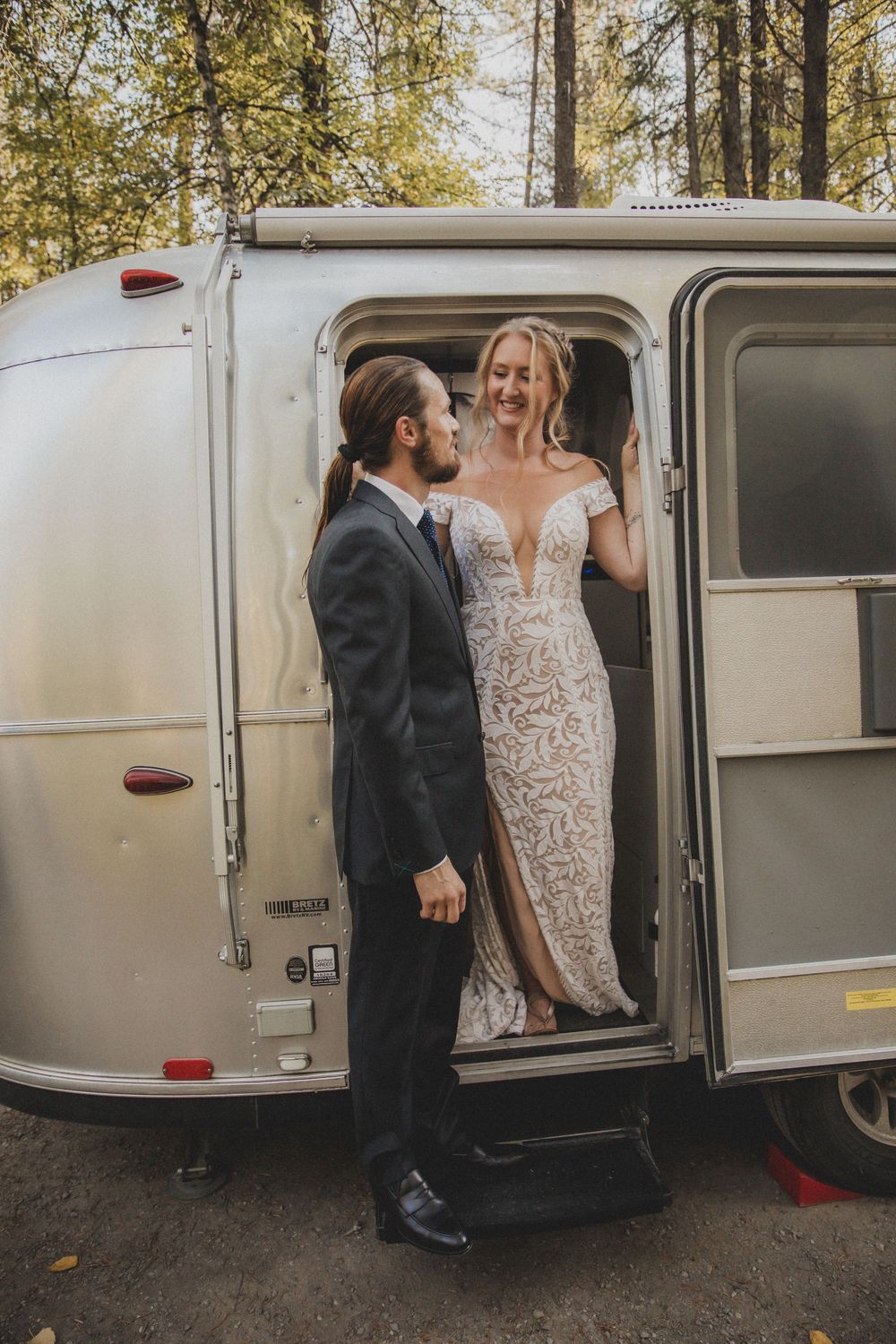 Wedding couple stepping into a vintage silver Airstream trailer surrounded by trees.