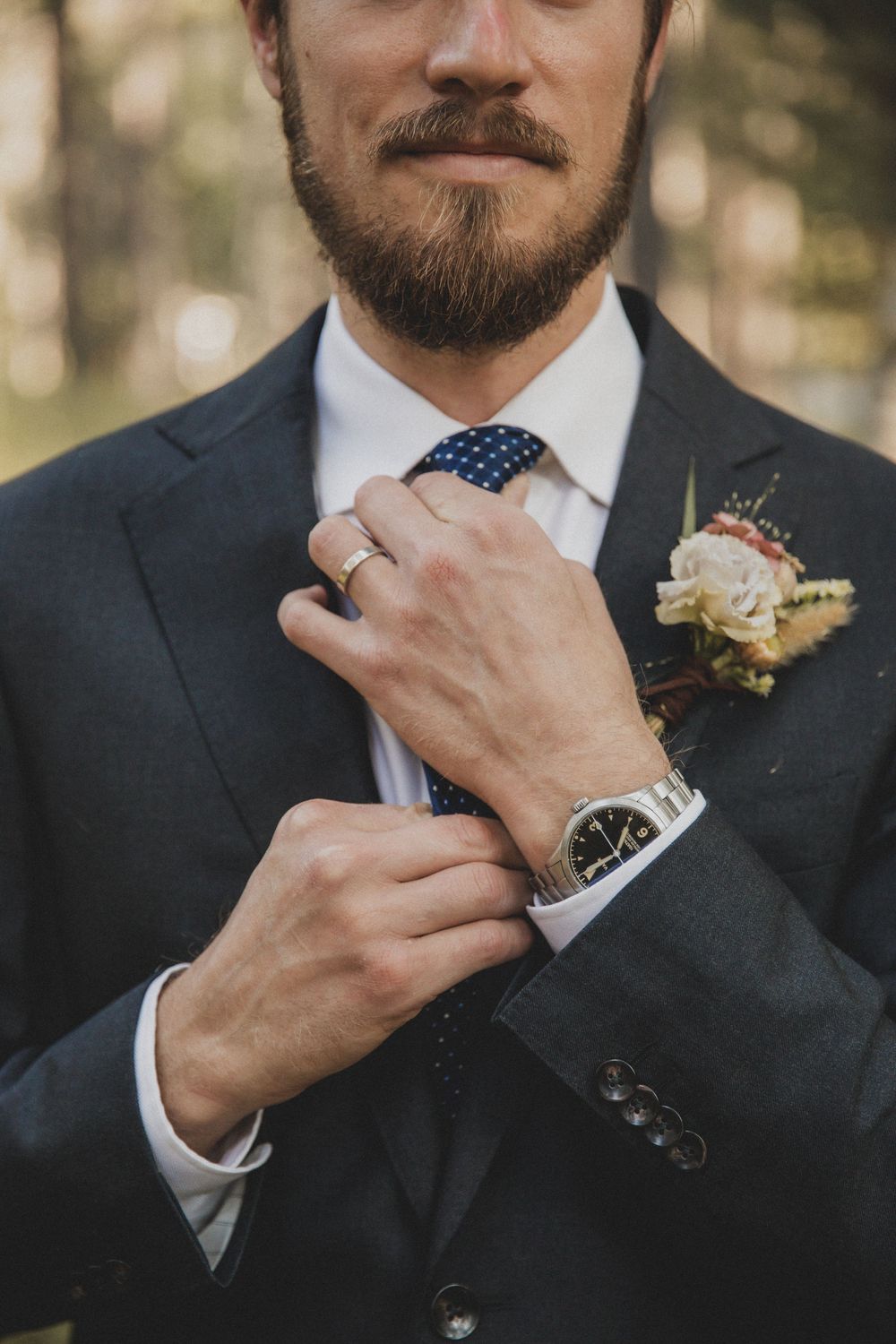Close-up shots of groom adjusting tie and boutonniere in formal black suit.