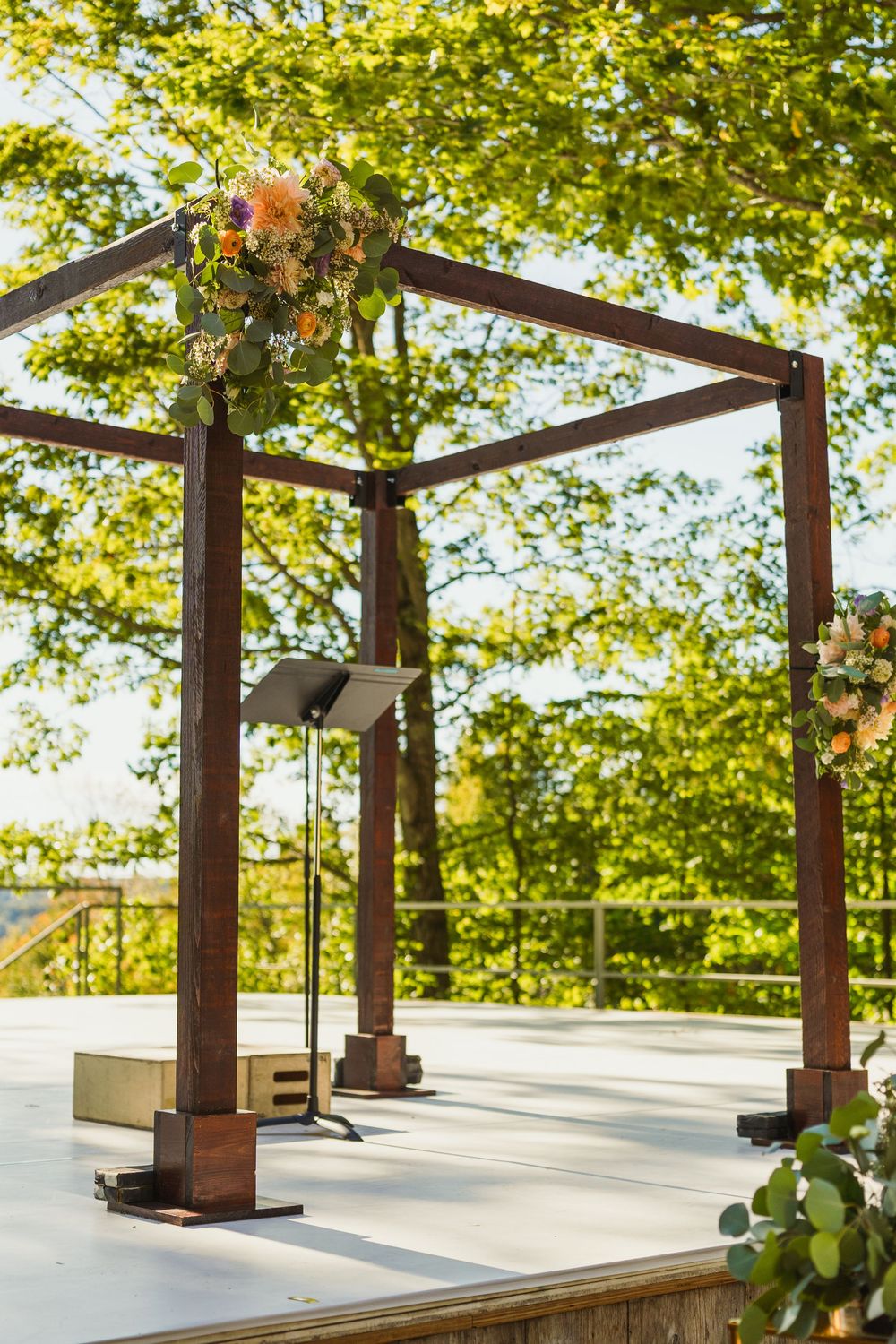 Rustic wooden wedding pergola with floral arrangements set against a backdrop of green trees.