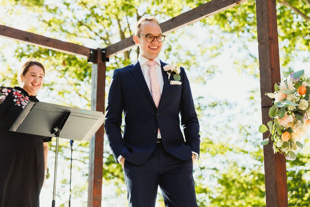 Wedding ceremony setup with wooden arbor decorated with floral arrangements in natural outdoor setting.
