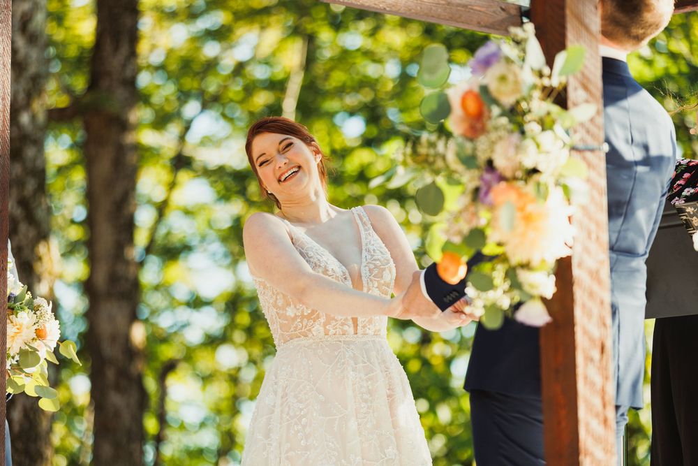 Wedding vows being exchanged beneath a wooden pergola adorned with peach and white flowers.