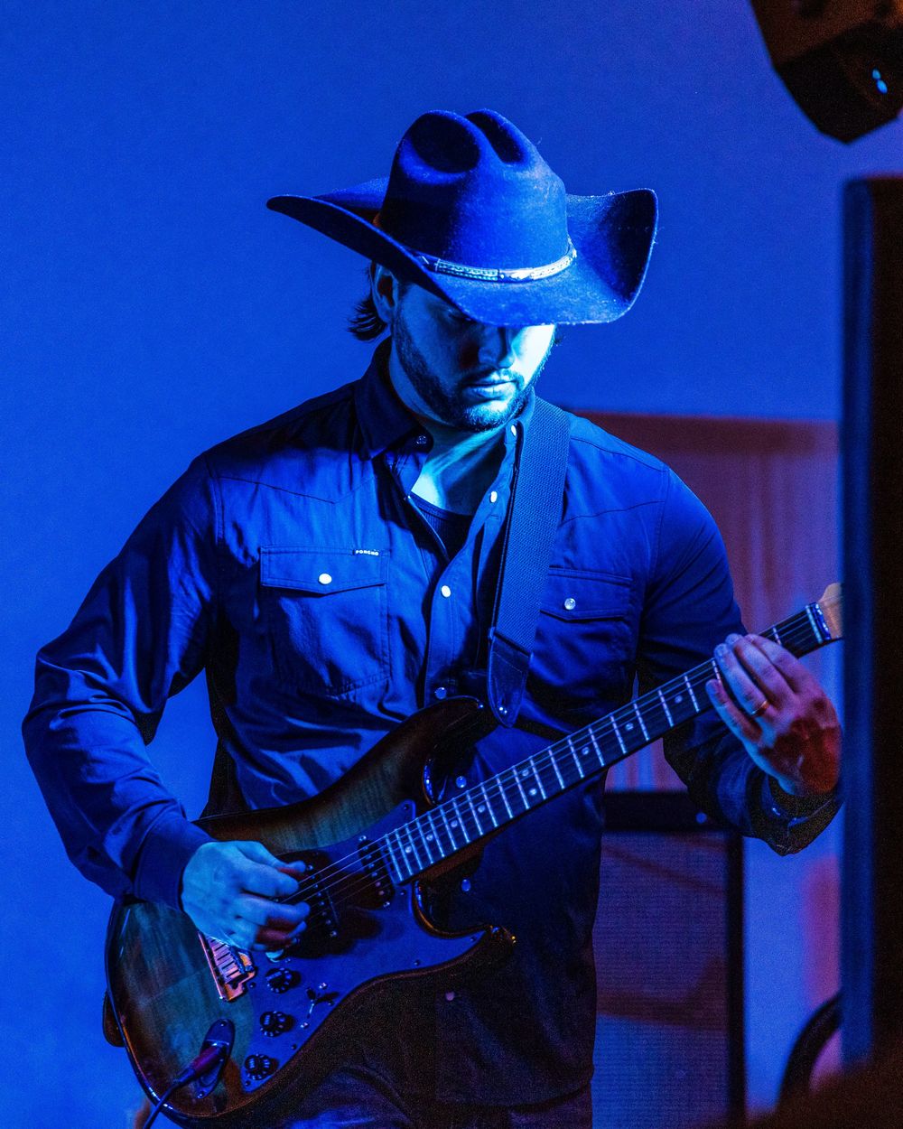 Musician playing guitar under dramatic blue stage lighting wearing cowboy hat. photography st louis