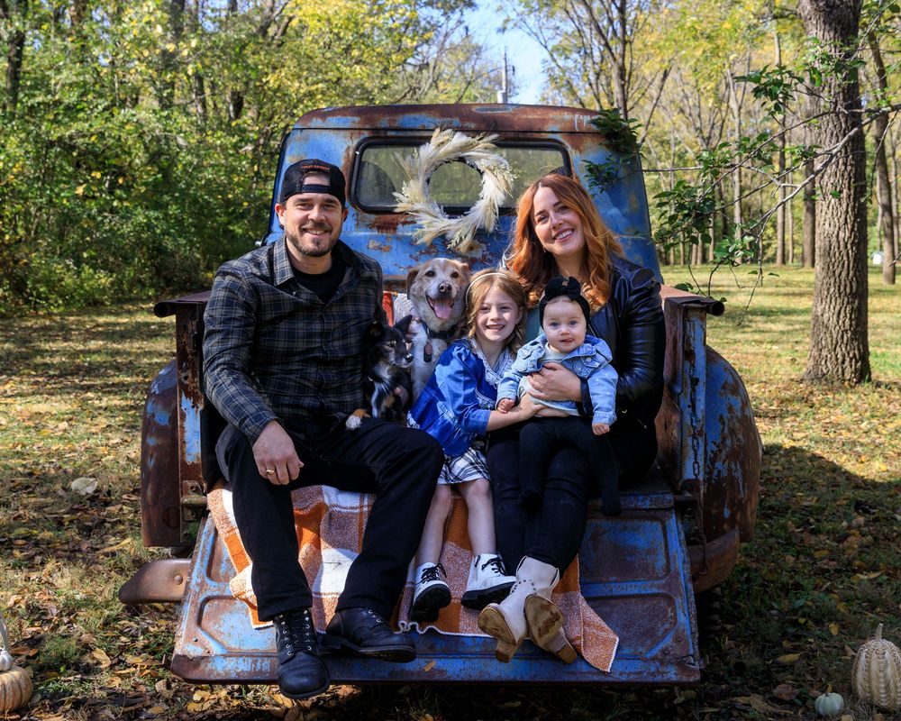 Family and dog relaxing together in back of pickup truck in autumn forest setting. photography st louis