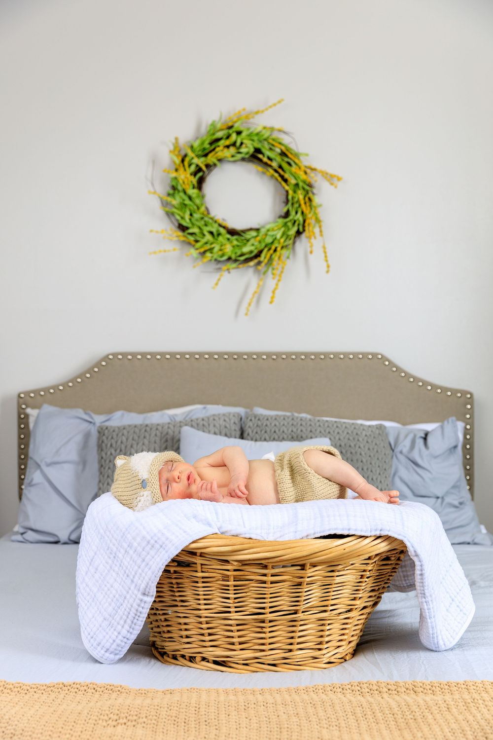 Neutral bedroom decor with wicker basket, grey headboard and green wreath on white wall. photography st louis.