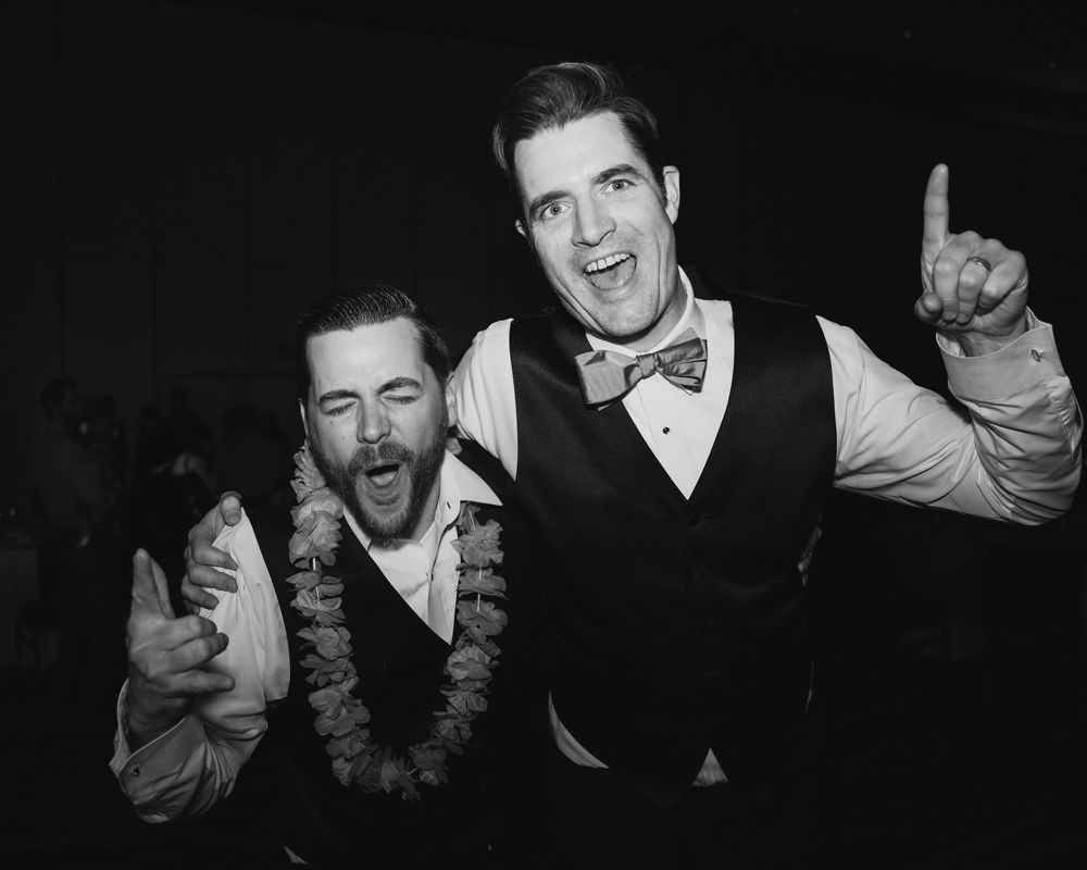 Two men in vests celebrating joyfully on the dance floor in a black and white wedding reception photo.at Sandia Resort and Casino