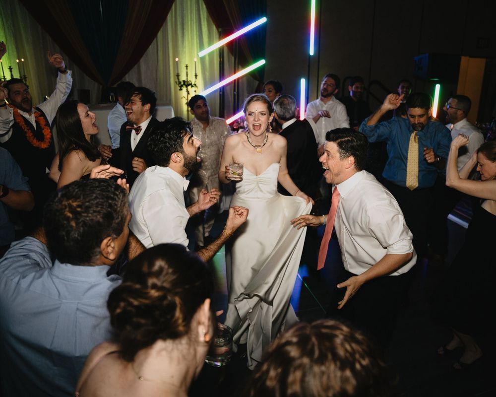 Bride in a white gown dancing joyfully surrounded by guests under colorful neon lights at her reception.at Sandia Resort and Casino