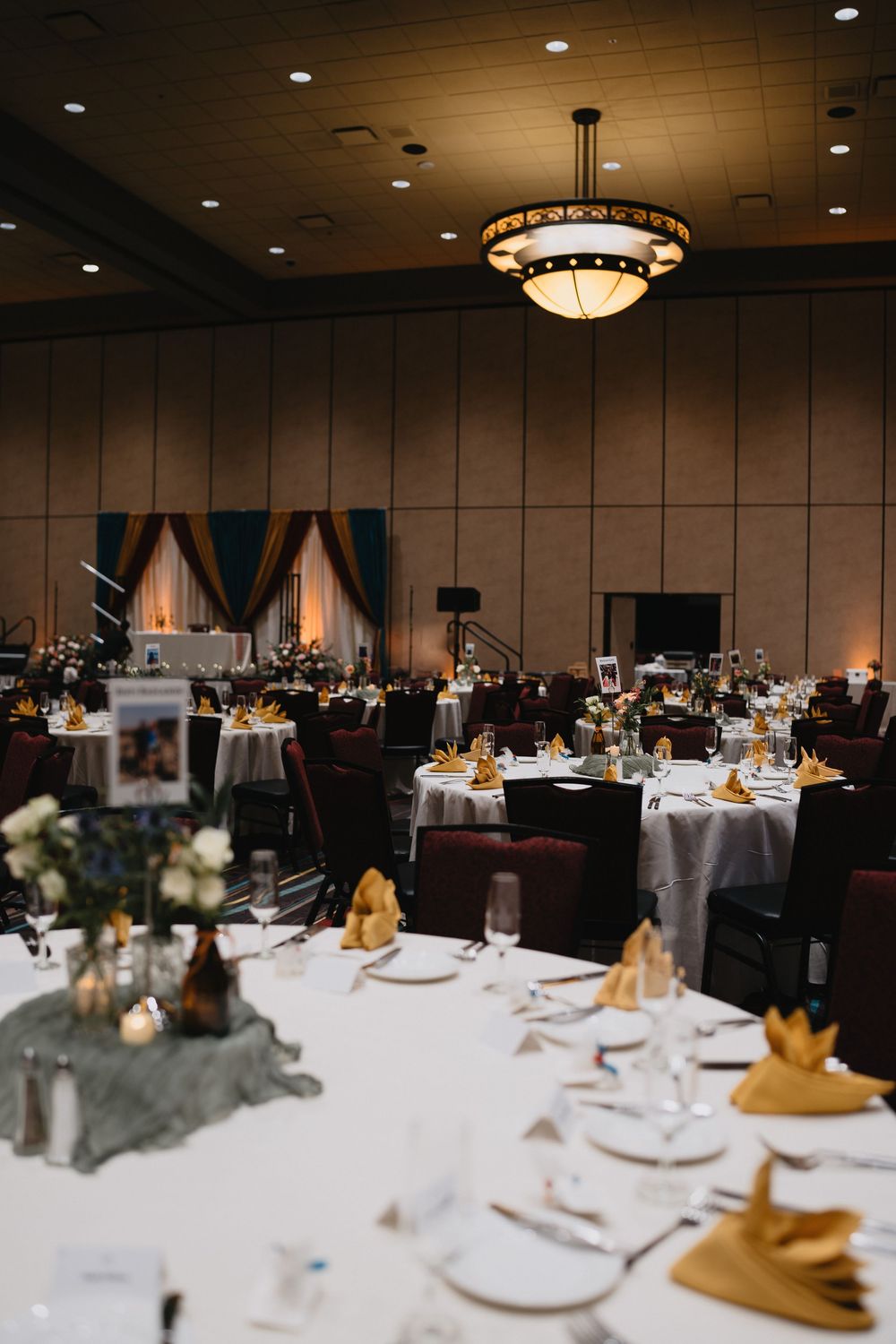 Elegant wedding reception ballroom with round tables, gold napkins, and floral centerpieces.