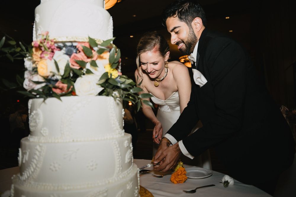 Smiling bride and groom cutting their elegant white tiered wedding cake decorated with colorful flowers.at Sandia Resort and Casino