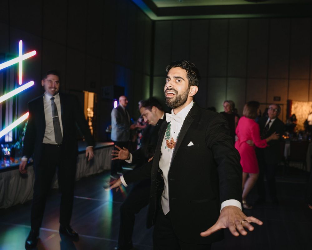 Groom dancing joyfully at wedding reception with colorful neon lights in background.at Sandia Resort and Casino