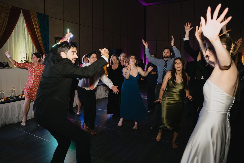 Wedding guests dancing enthusiastically with hands raised on a lively reception dance floor.