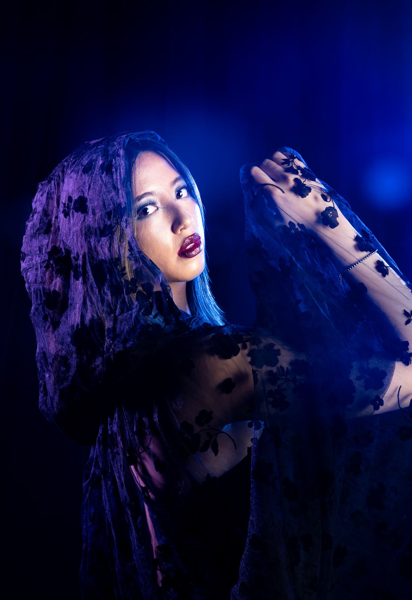 Melinoë, Goddess of Ghosts & Nightmares , pulled back shot, girl with a black cape (hood on) with blue and purple LED lights