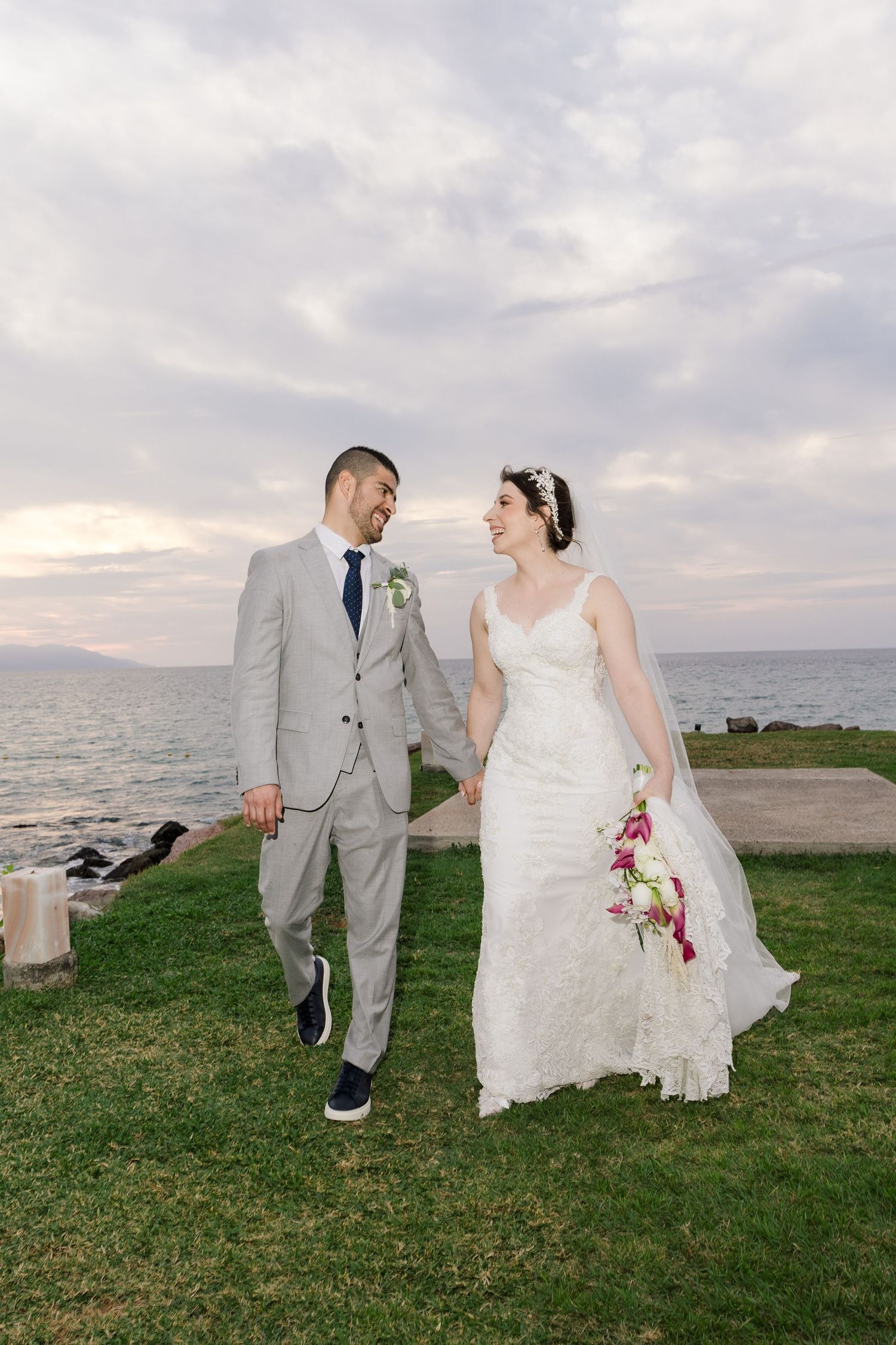 Una pareja en su boda camina junta por un pintoresco jardín frente al mar al atardecer en Puerto Vallarta.