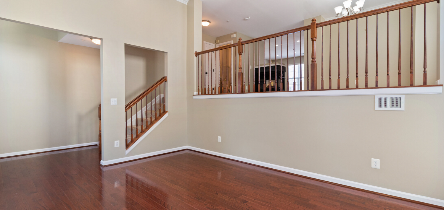 Empty room interior with hardwood floors and wooden stair railing leading to upper level.