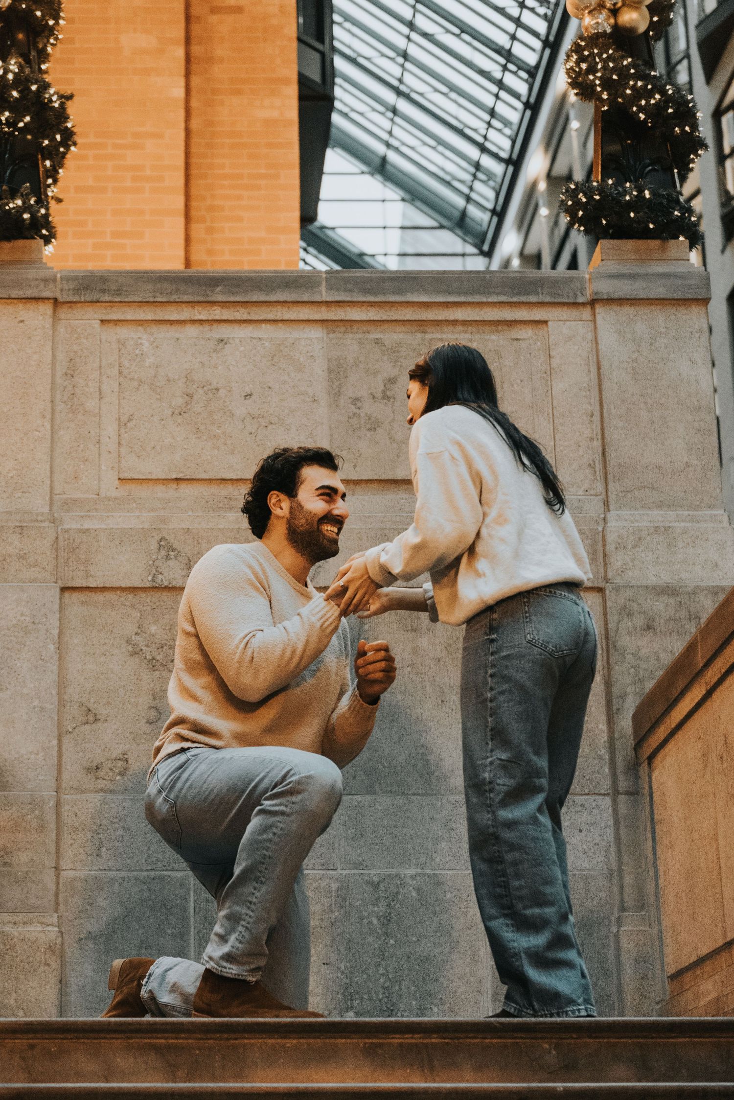 Three sequential photos showing a romantic proposal moment on stone steps with warm lighting and glass ceiling above.