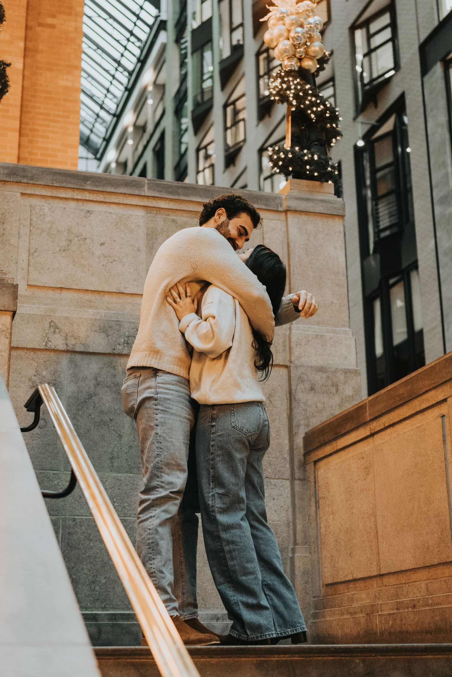 A couple shares an intimate moment on stone steps with twinkling lights in the background.