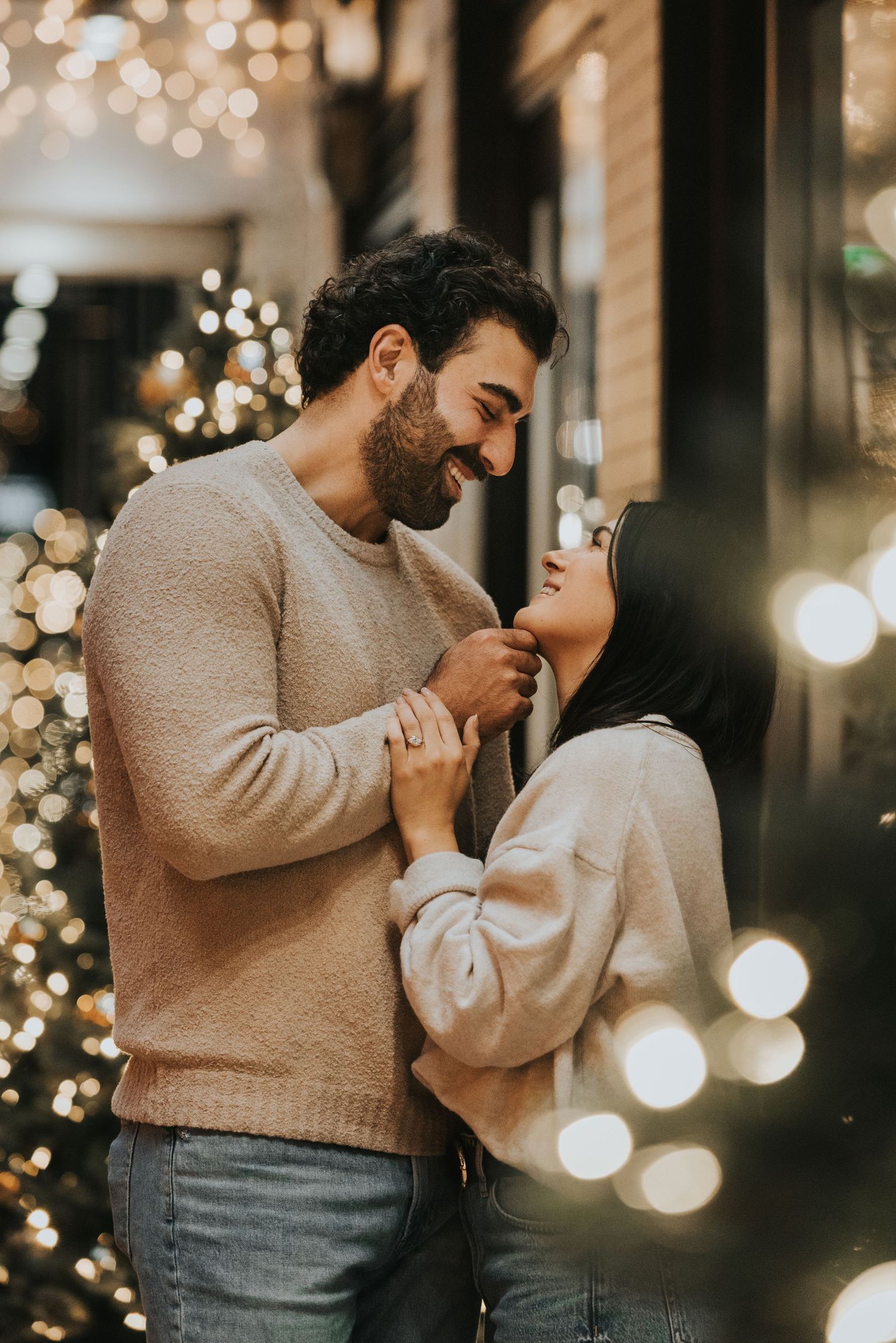 Romantic couple in cozy sweaters share an intimate moment against a backdrop of twinkling holiday lights and bokeh effects.