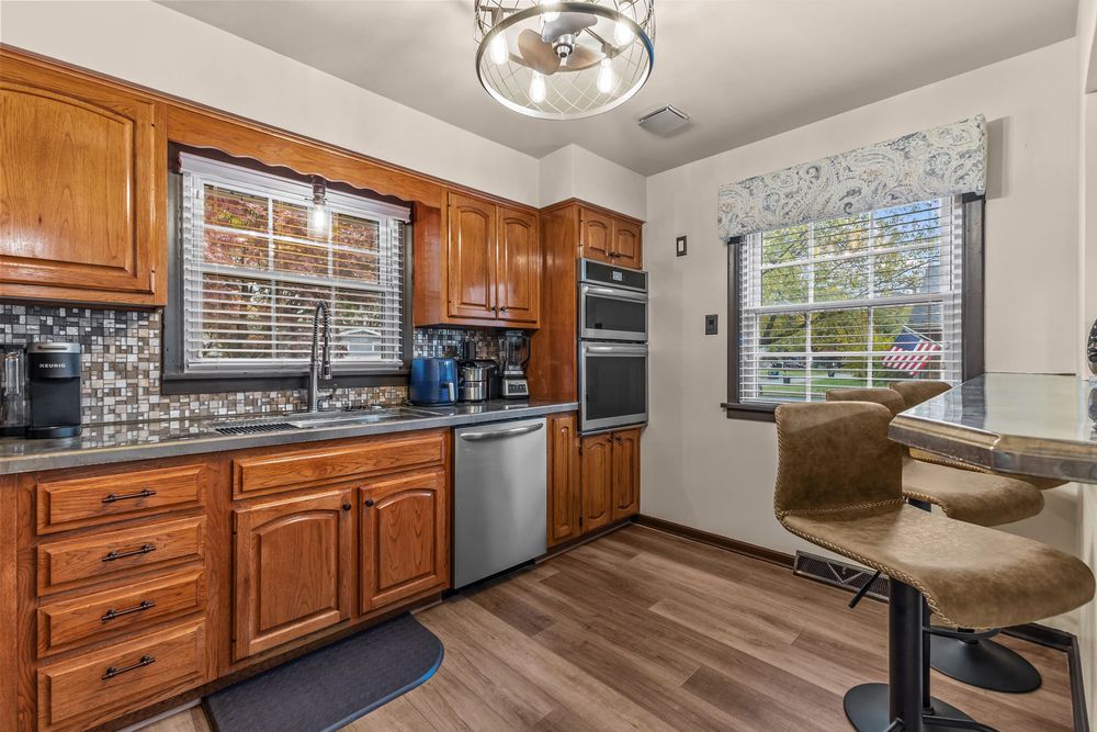 Kitchen with brown cabinets, stainless steel appliances, mosaic tile backsplash, and hardwood floors.