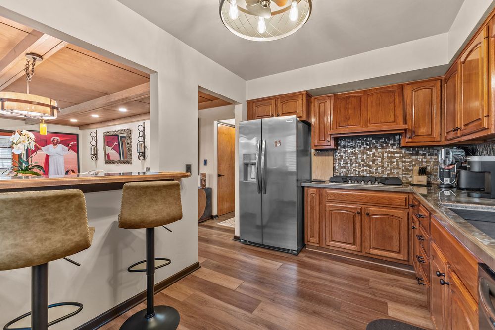 Kitchen featuring stainless steel refrigerator, brown cabinets, dark countertops, and hardwood floors.
