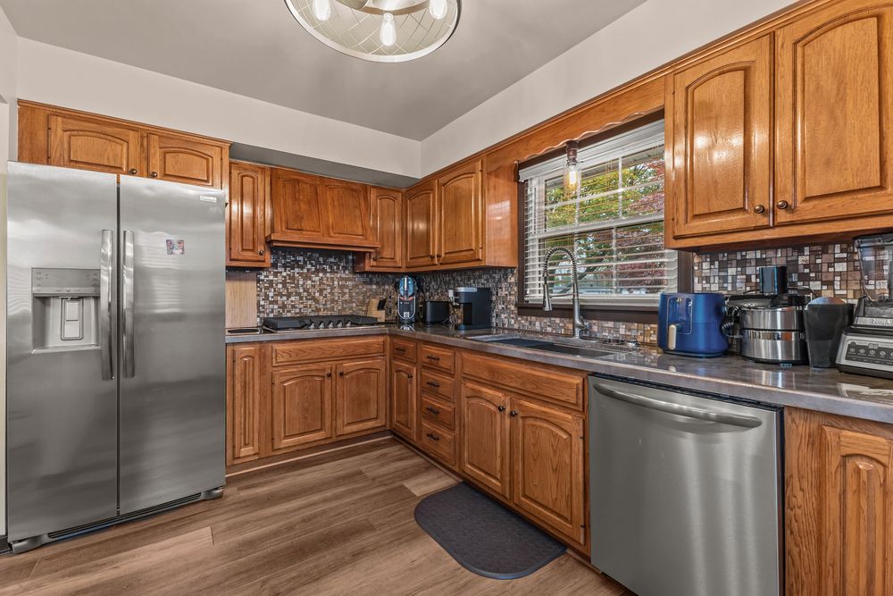 Kitchen with stainless steel appliances, brown cabinetry, mosaic backsplash, and dark countertops.